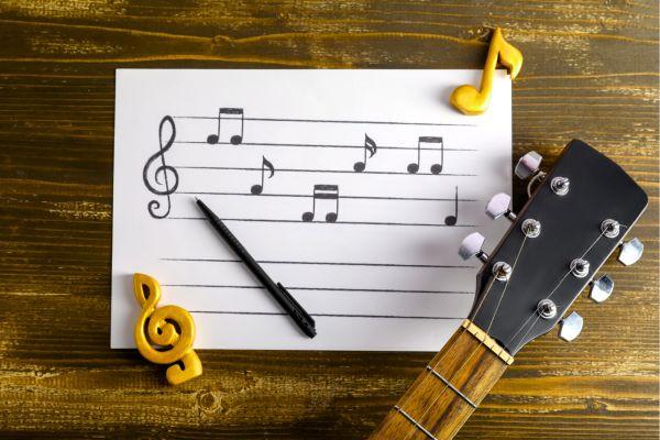 Music notation paper with notes written on it and a pen, with the fret of a guitar lying next to the paper