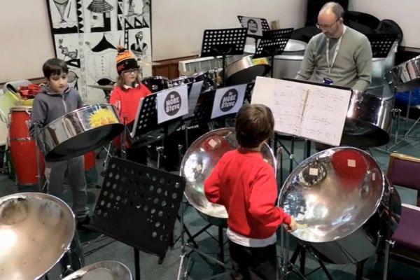 3 young people playing music on steel pans with their teacher
