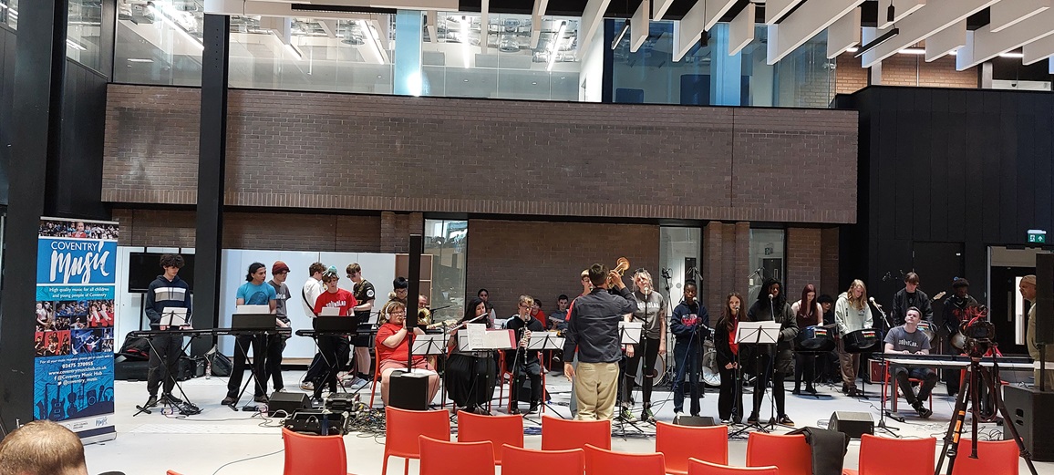 teenage children standing around with a mixture of instruments rehearsing for a performance