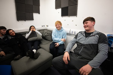 happy teenage students chilling on a sofa with Ed Sheeran