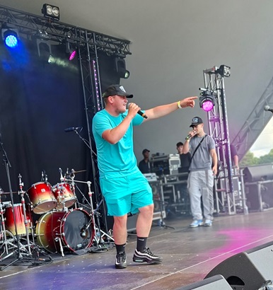 young boy wearing blue rapping and pointing at the crowd on a stage at a festival