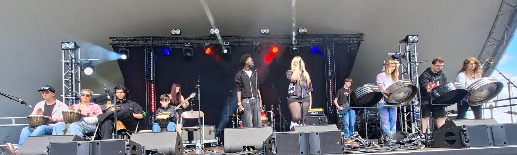 Teenage musicians performing on a range of musical instruments on a large stage at a festival