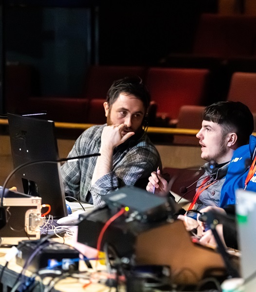young person smiling with member of staff behind the tech desk in a theatre
