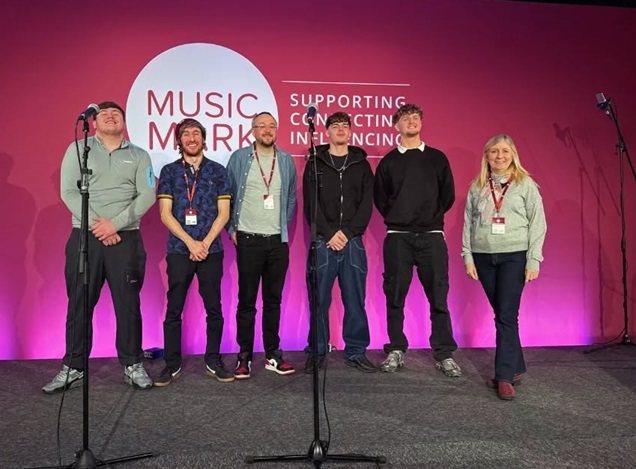 Coventry Music team posing for a photograph on a stage behind microphones at a music conference