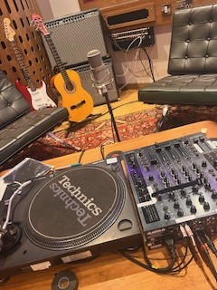 an image of a dj deck, guitar and other instruments in a cosy living room with sofas