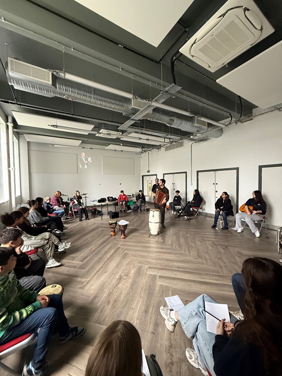 Music teacher standing behind a large drum on a room surrounding my pupils with smaller drums and other instruments