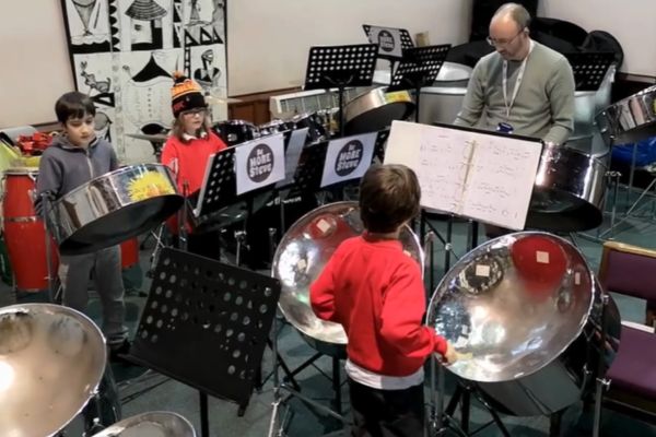 3 young people playing music on steel pans with their teacher