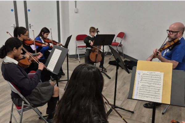 A group of young musicians playing violins sitting in a semi circle around a music teacher